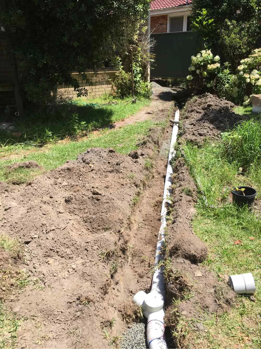 New drainage pipe laid along a residential garden trench during a plumbing line installation on the Central Coast
