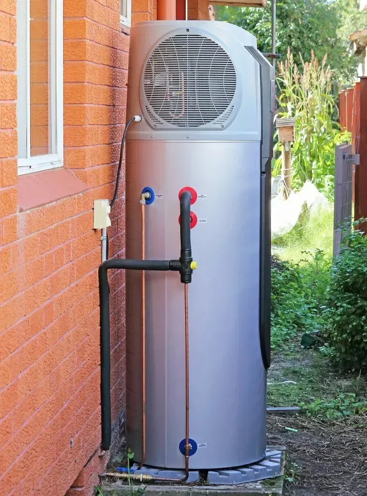 Silver heat pump hot water system installed beside a brick wall