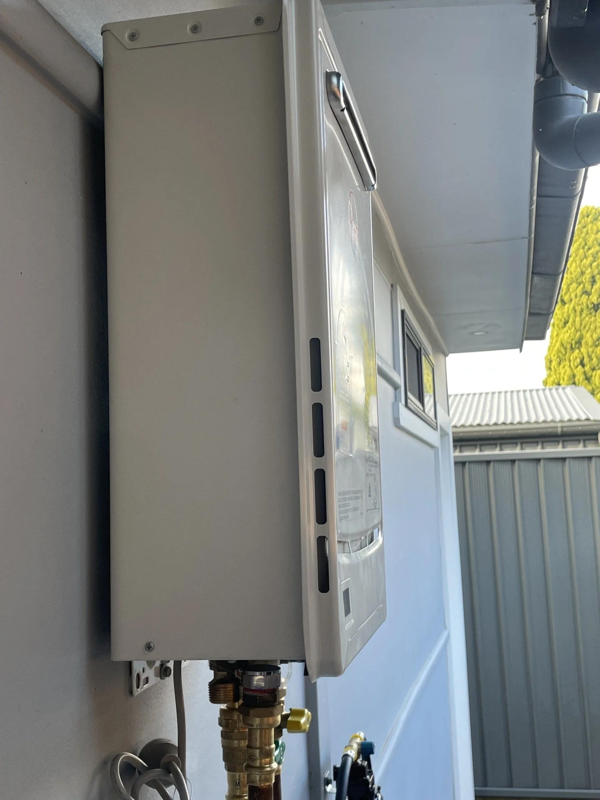 Outdoor continuous flow hot water unit installed on the side of a house