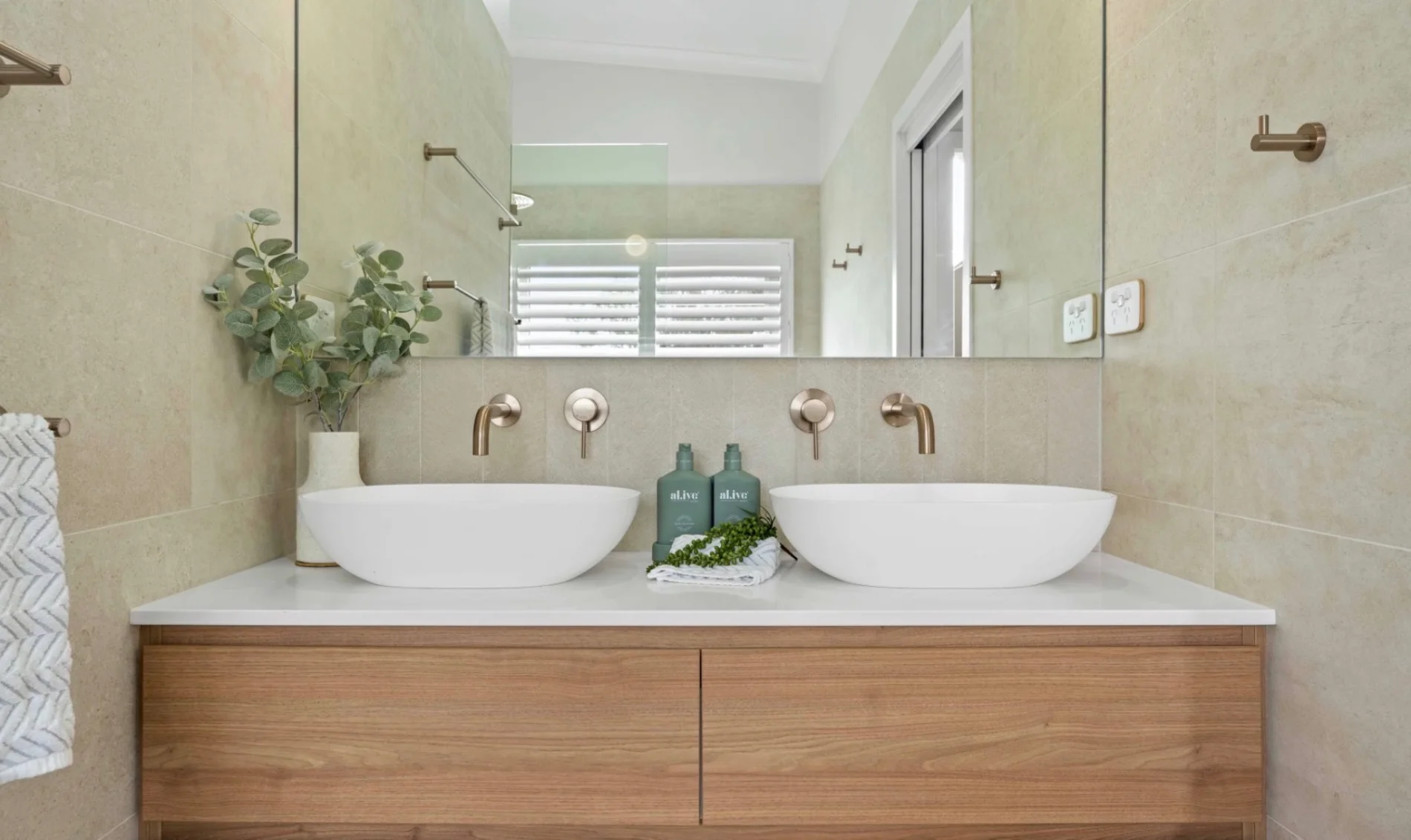 Double vessel sink vanity with brushed nickel tapware and stone tile walls in a renovated bathroom by AH Plumbing & Maintenance