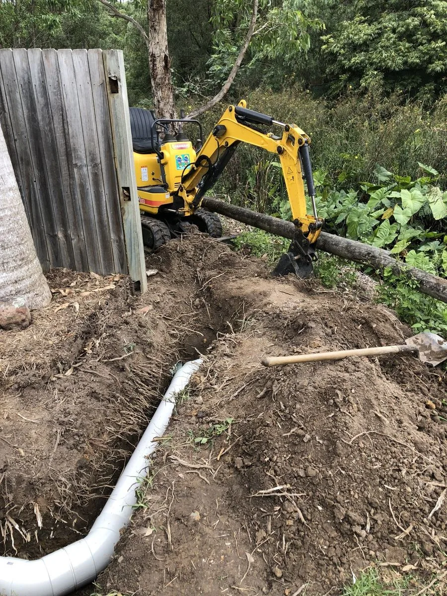 Kubota mini excavator digging a trench against a timber fence at a residential property