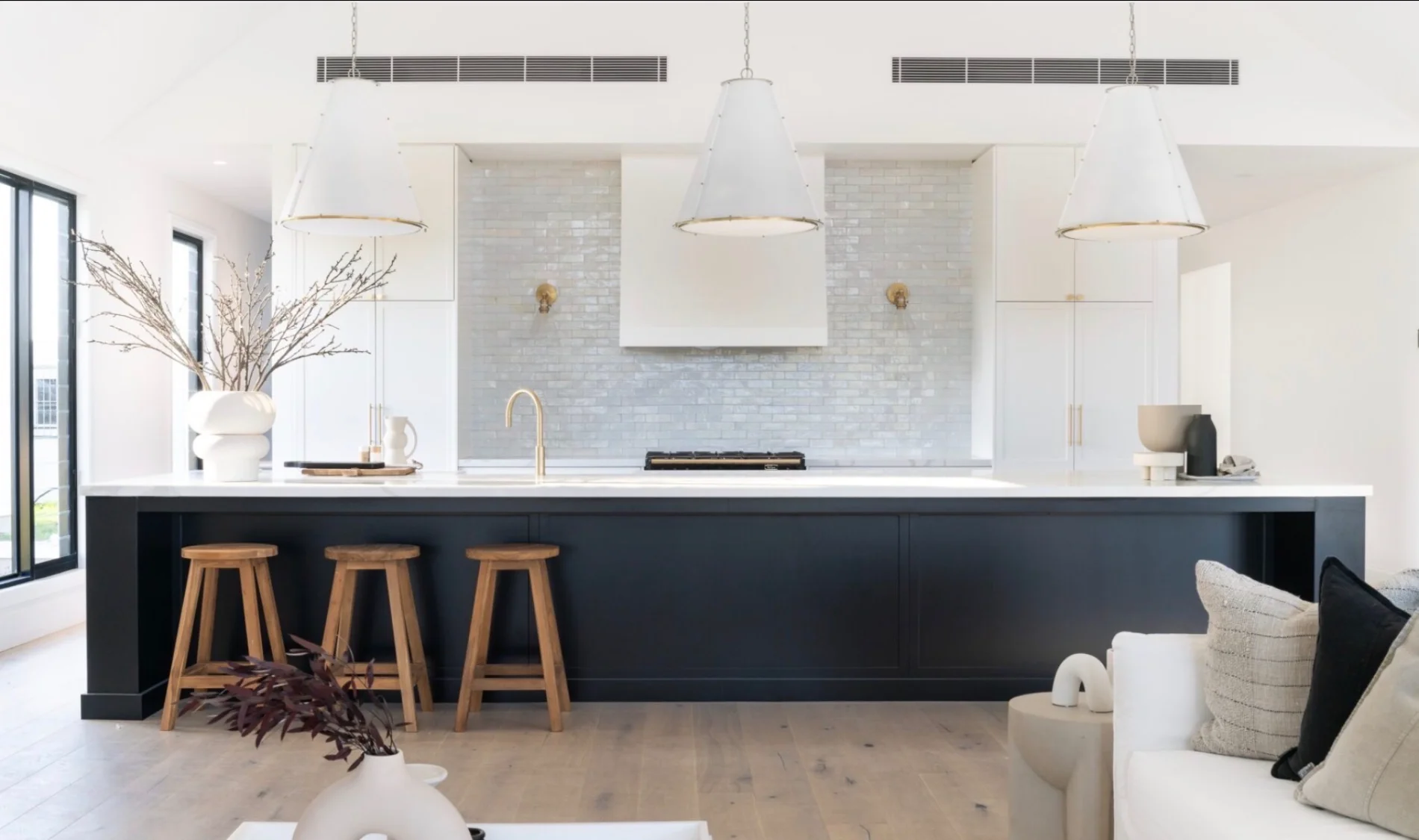 Modern kitchen island with dark cabinetry, gold tapware, pendant lighting and timber bar stools
