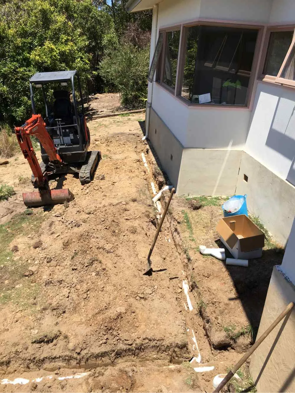 Mini excavator working in a confined space beside a house during a tight access excavation