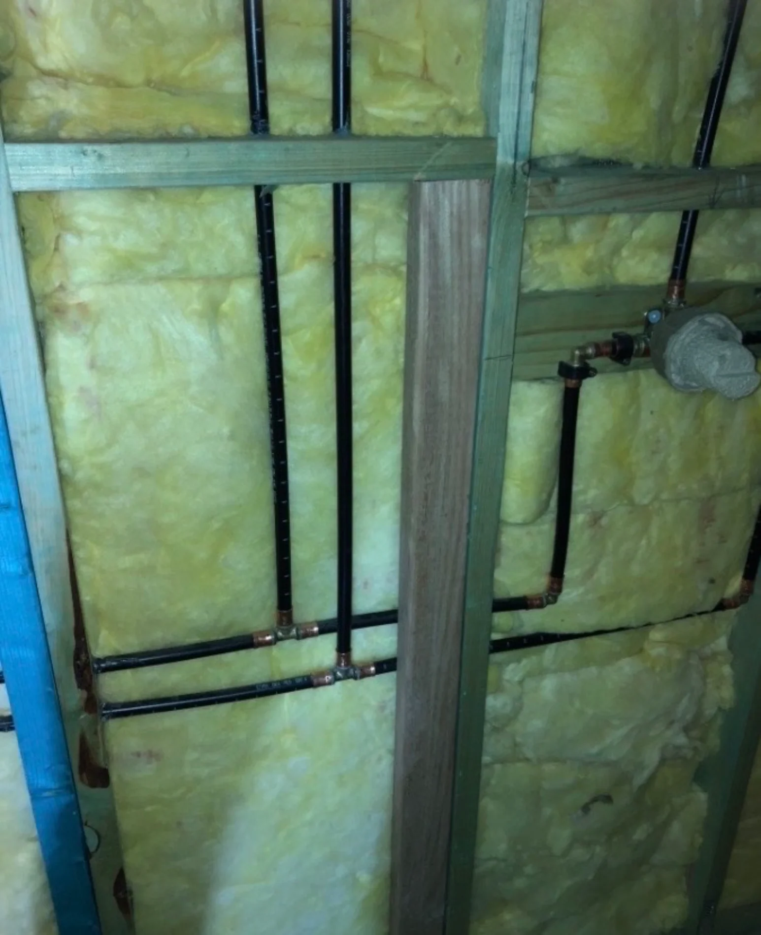 Hot and cold water pipe rough-in with copper and black piping installed through wall framing and insulation