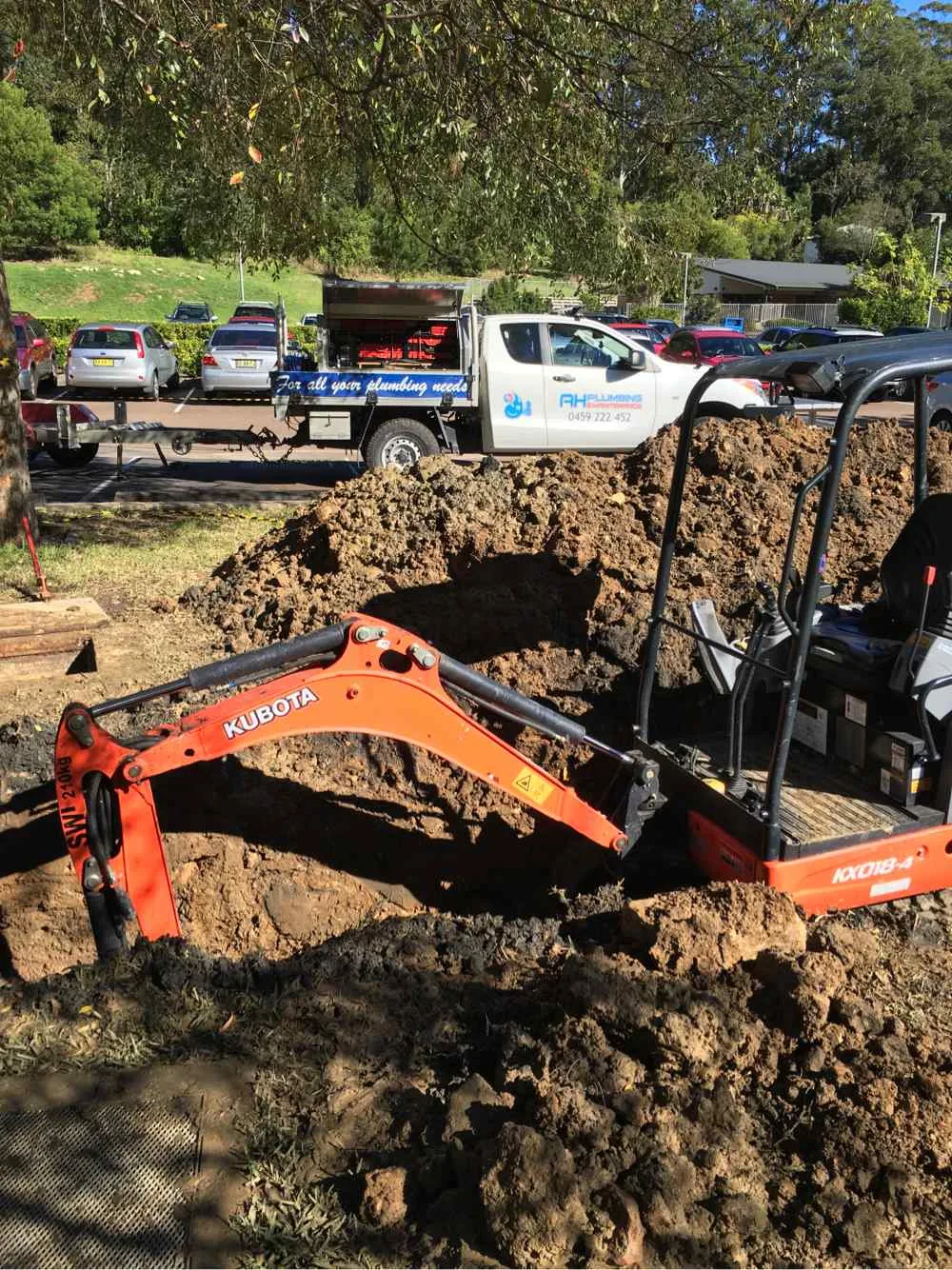 Kubota mini excavator digging beside an AH Plumbing branded ute at a residential excavation job