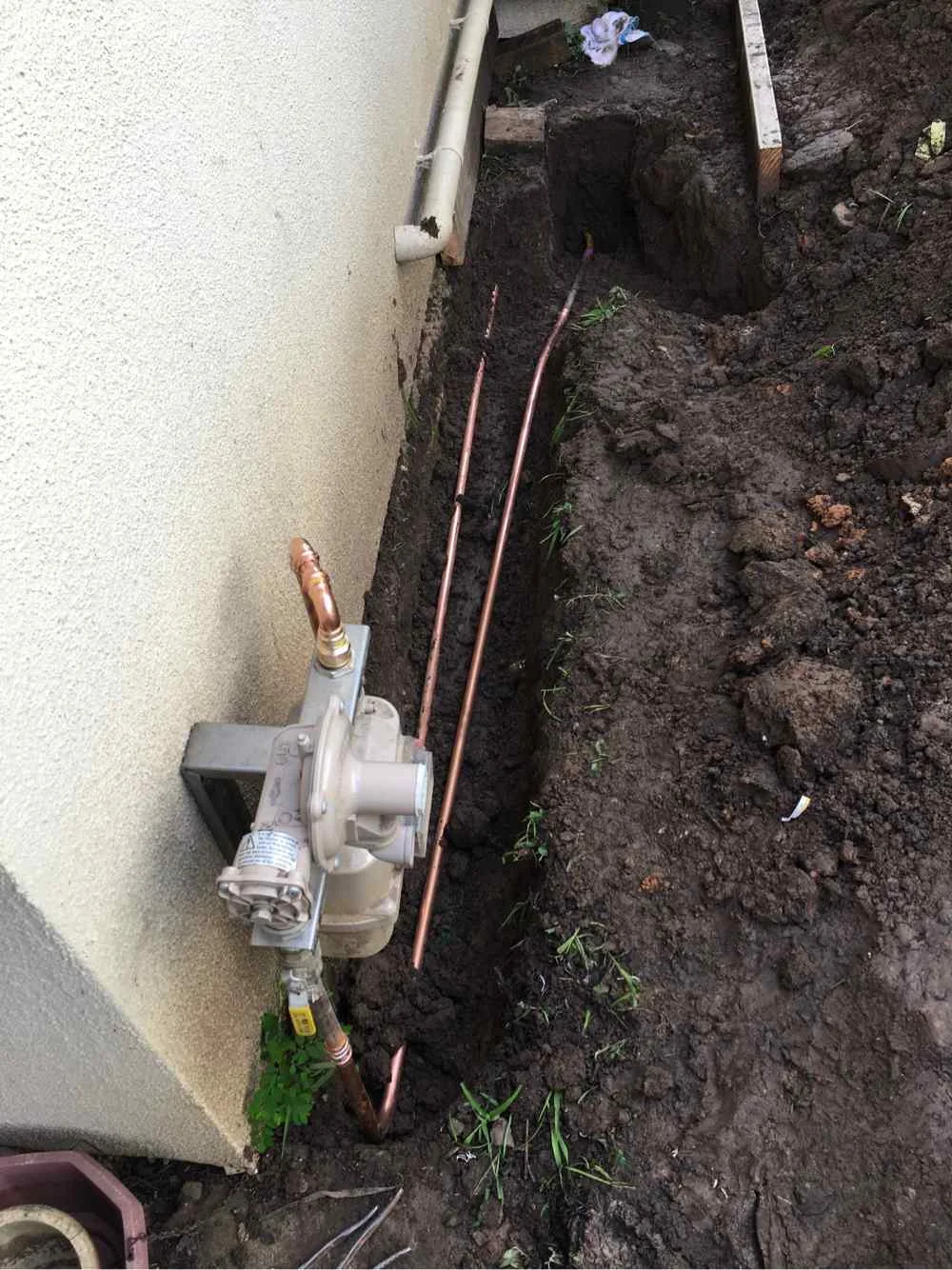 Copper gas pipe and regulator connection laid in a trench beside a rendered house wall