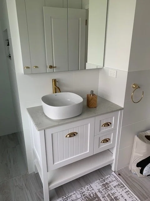 White shaker-style vanity with round vessel sink, gold tapware, and mirrored cabinet