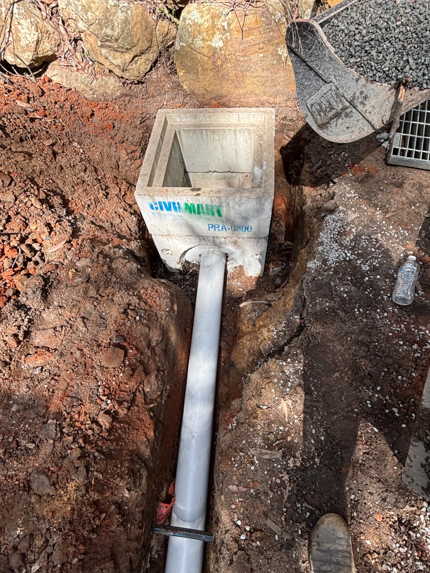 Concrete stormwater pit and drainage pipe installed in a rocky excavation trench on the Central Coast