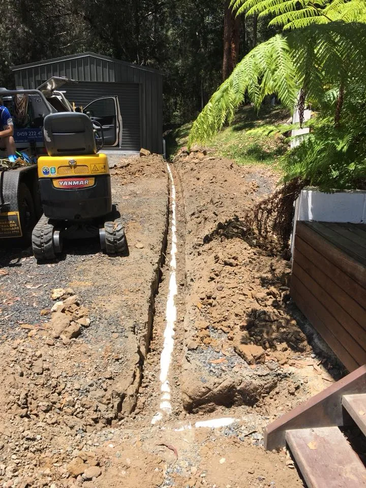 Yanmar mini excavator beside a freshly laid pipe in a narrow trench at a bush residential property