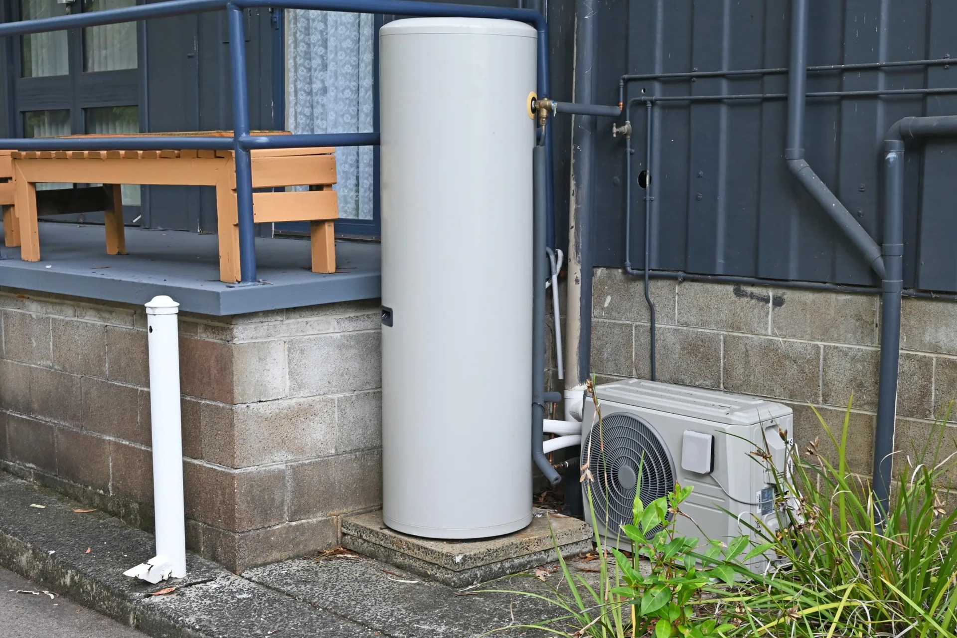 Outdoor hot water storage tank beside a house with exposed pipework